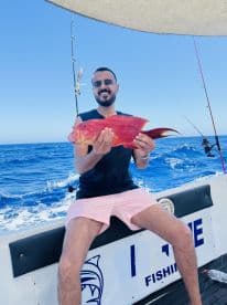 A proud angler displays a vibrant catch while fishing on a boat in the open ocean, showcasing the thrill of a successful fishing trip.
