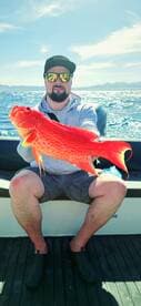 A proud angler displays a vibrant red fish caught during a fishing trip, showcasing the thrill of the catch on the open water.