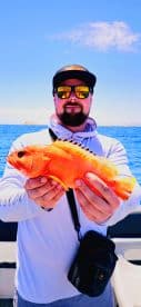 A proud angler displays a vibrant orange fish caught while fishing at sea, showcasing the thrill of a successful catch.