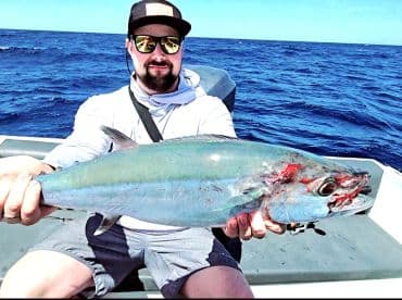 A proud angler displays his impressive catch while fishing in the open ocean, showcasing the thrill of deep-sea fishing adventures.