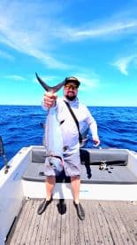 A proud angler holds up a freshly caught fish aboard a boat in the open ocean, showcasing the thrill of fishing adventures.
