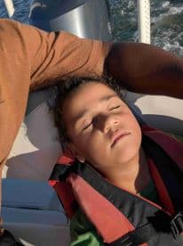 A child peacefully sleeps in a life jacket on a boat, capturing a serene moment during a day on the water.