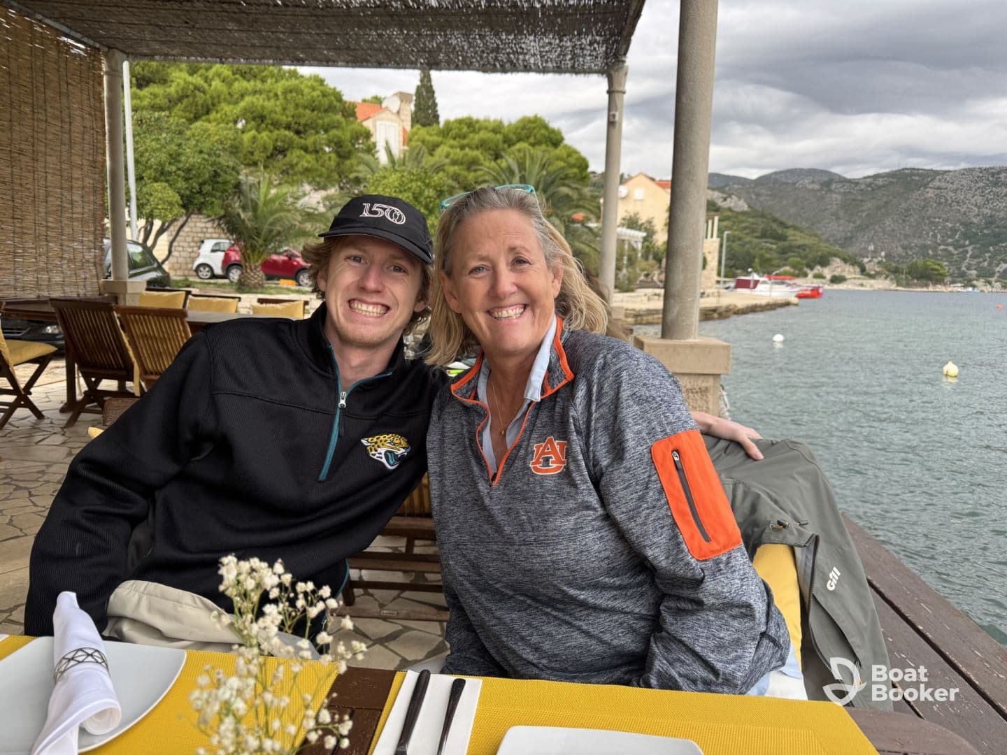 A joyful moment captured of a mother and son enjoying a meal together at a waterfront restaurant, surrounded by scenic views — perfect for family bonding on vacation.