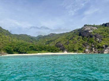 A stunning view of a secluded beach surrounded by lush greenery and rocky hills, perfect for island hopping and exploring pristine coastlines.