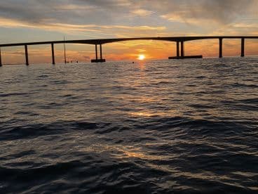 A stunning sunset view over the water, framed by a bridge, creating a picturesque scene perfect for evening cruises.