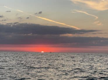 A stunning sunset over the ocean, with a distant boat silhouetted against the vibrant sky — perfect for capturing the beauty of evening cruises.