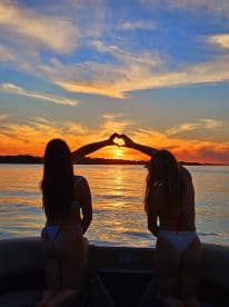 Two friends create a heart shape with their hands against a stunning sunset backdrop while enjoying a boat ride — a perfect moment for friendship and celebration on the water.