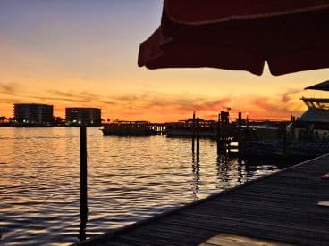 A stunning sunset over the harbor, with boats docked and buildings silhouetted against the colorful sky — a perfect backdrop for evening cruises.