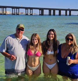 A joyful group of four enjoys a sunny day at the beach, wading in the clear water — perfect for family fun and memorable summer outings.