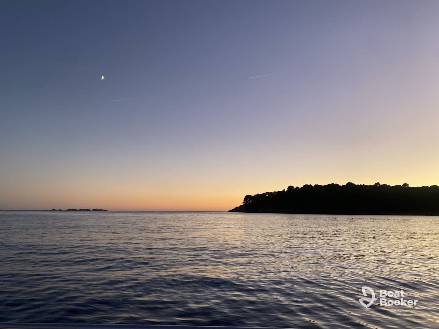 A serene sunset view over calm waters, showcasing the coastline and a crescent moon — perfect for tranquil evening boat rides.