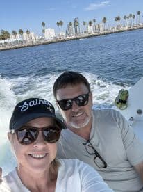 A couple enjoys a sunny day on the water, capturing a selfie with a vibrant city skyline in the background — perfect for memorable boating adventures.