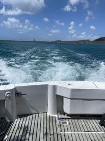 A view from the back of a boat cruising through clear waters, showcasing the boat's wake and the scenic landscape ahead.