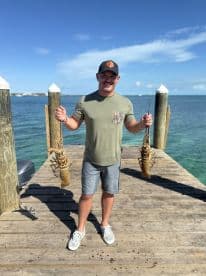 A man proudly displays his catch of lobsters on a sunny day at the pier, showcasing the excitement of a successful fishing trip.