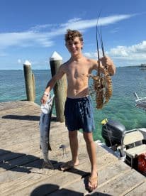 A young boy proudly displays his catch of the day, featuring a fish and lobsters, showcasing the excitement of a successful fishing trip.