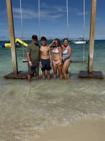 A joyful family poses together on a beach swing in shallow water, capturing a fun-filled day under the sun — perfect for memorable beach outings.