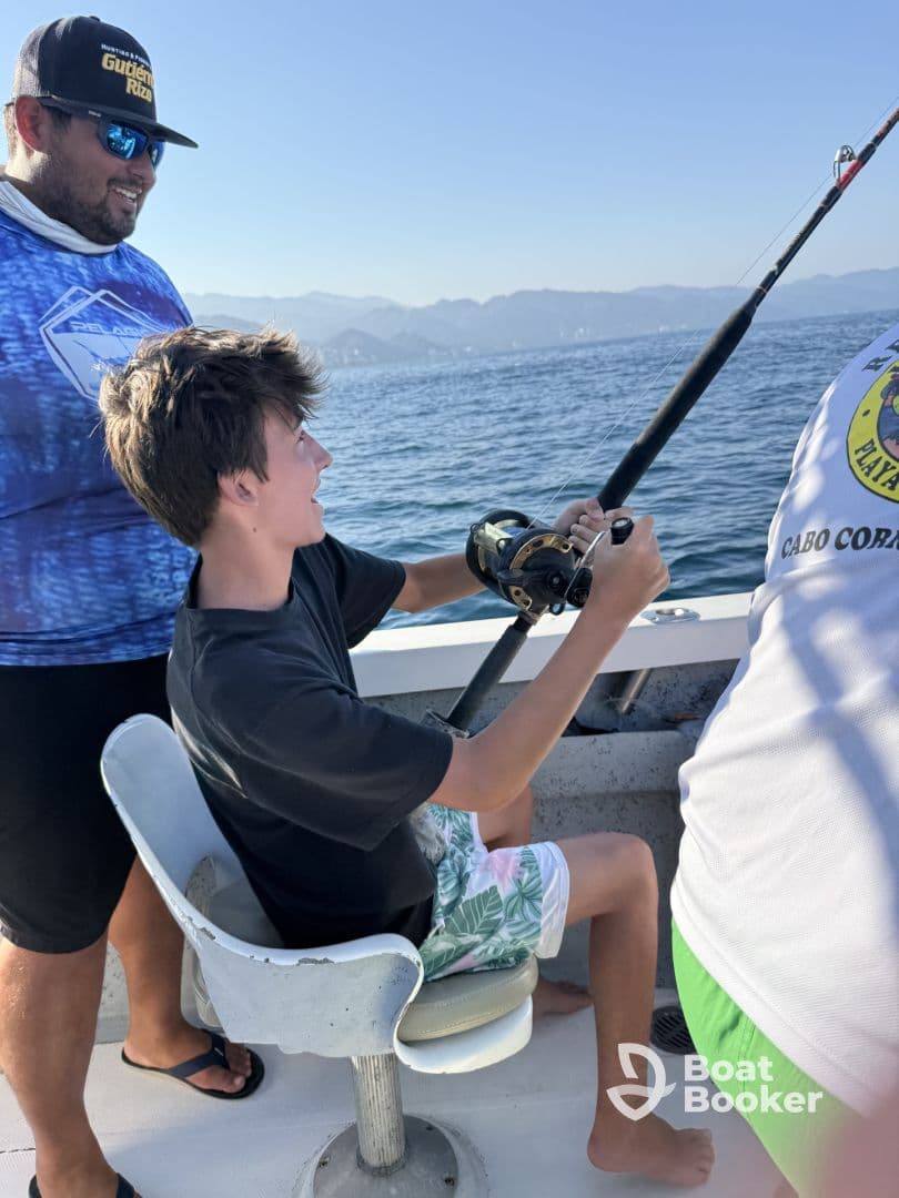 A young boy enjoys fishing on a boat, guided by an adult, capturing the excitement of a day on the water.