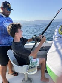A young boy enjoys fishing on a boat, guided by an adult, capturing the excitement of a day on the water.