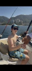 A young boy proudly holds a fish while fishing on a boat, showcasing the excitement of a day out on the ocean.