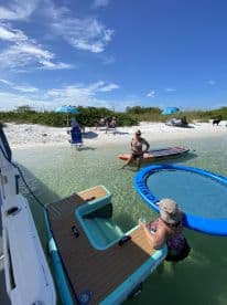 A lively group enjoys a beach day with paddleboards and relaxation in shallow waters, perfect for summer fun and outdoor adventures.