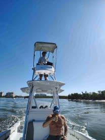 Two friends enjoy a day on the water, one steering the boat while the other relaxes with a drink — perfect for a fun day out on the sea.
