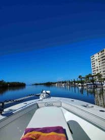 A serene view from the front of a boat named 'Conch', gliding through calm waters lined with docks and palm trees, perfect for a relaxing day on the water.