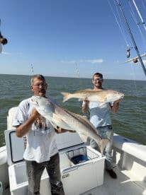 Two anglers proudly display their impressive catch while fishing on a boat, showcasing the excitement of a successful day on the water.