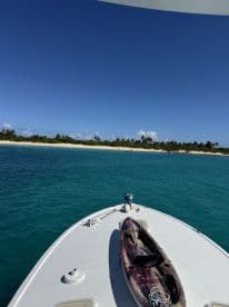 A stunning view from the bow of a boat featuring a kayak, with a picturesque beach and clear turquoise waters in the background — perfect for adventure seekers and water enthusiasts.