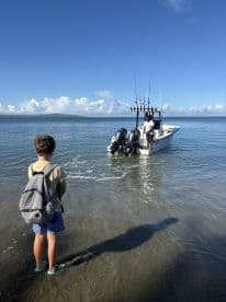 A child stands on the beach watching a fishing boat approach, creating a perfect moment of anticipation for a day on the water.