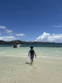 A child walks along the sandy beach towards a boat anchored in the clear turquoise waters, capturing a serene moment in a tropical paradise.