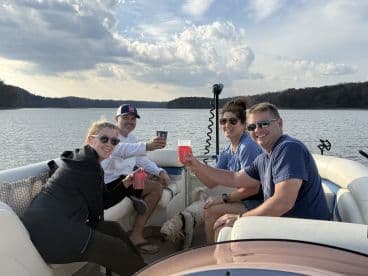 A cheerful group enjoys drinks on a pontoon boat, celebrating together on the water — perfect for gatherings and fun outings.