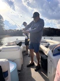Two friends enjoy a day of fishing on a pontoon boat, showcasing the thrill of catching fish on a serene lake.
