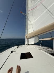 A close-up view of a sailboat's deck with feet visible, showcasing the serene experience of sailing on open waters.
