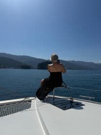 A woman enjoys a serene moment on the deck of a boat, overlooking the stunning ocean and mountainous backdrop — perfect for relaxation and scenic views.