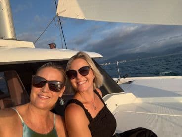 Two friends enjoy a sunset sailing experience on a yacht, capturing a joyful moment at sea.