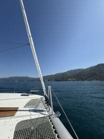 A stunning view from the bow of a catamaran, showcasing the clear blue waters and lush mountainous backdrop — perfect for sailing adventures.