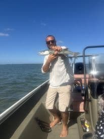 A man proudly displays his catch while fishing on a boat, showcasing the thrill of a successful day on the water.