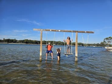 A fun-filled moment with friends enjoying a swing in shallow water, capturing the essence of summer adventures by the lake.