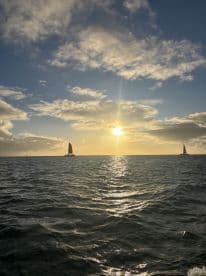 A breathtaking sunset over the ocean with sailboats in the distance, capturing the serene beauty of a sailing adventure.