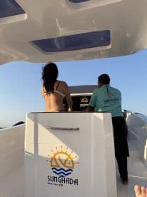 A view of the helm area inside a boat, featuring two individuals preparing for a tour. The boat's branding is visible, indicating a professional boat tour service.