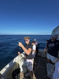 A young angler proudly displays his catch while fishing with friends on a boat, capturing the excitement of a day on the ocean.