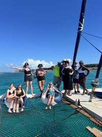 A lively group enjoys a day on a catamaran, soaking up the sun and celebrating together in the beautiful turquoise waters.