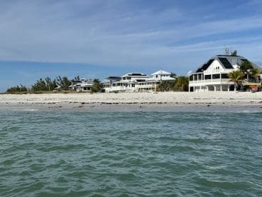 A view of beachfront properties with a sandy shore and clear water, capturing a serene coastal landscape.
