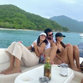 A joyful group of friends relaxes on a boat, enjoying drinks and the scenic backdrop of lush mountains — perfect for a fun day on the water.