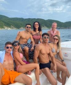 A lively group of friends enjoys a fun day on the boat, soaking up the sun and celebrating together against a stunning coastal backdrop.