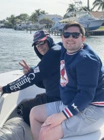 Two friends enjoy a sunny day on the water, smiling and posing for the camera while aboard a boat — a perfect moment for friendship and adventure.