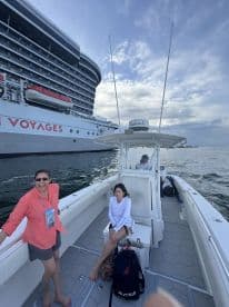Two guests enjoy a relaxing moment aboard a boat, with a large cruise ship in the background, showcasing the perfect blend of adventure and leisure on the water.