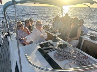 A lively group enjoys a sunset cruise on a sailboat, celebrating with drinks and laughter as the sun sets over the ocean.