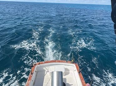 A view from the back of a fishing boat as it navigates through deep blue waters, showcasing the vessel's structure and the wake it creates.