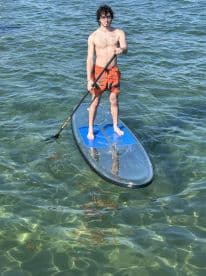 A young man paddleboards in clear waters, showcasing an active and adventurous day on the water — perfect for water sports enthusiasts.