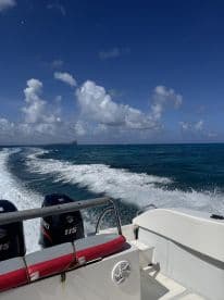A dynamic view from the back of a speedboat cruising through vibrant blue waters, showcasing the boat's powerful engines and the scenic backdrop of clouds and distant land.